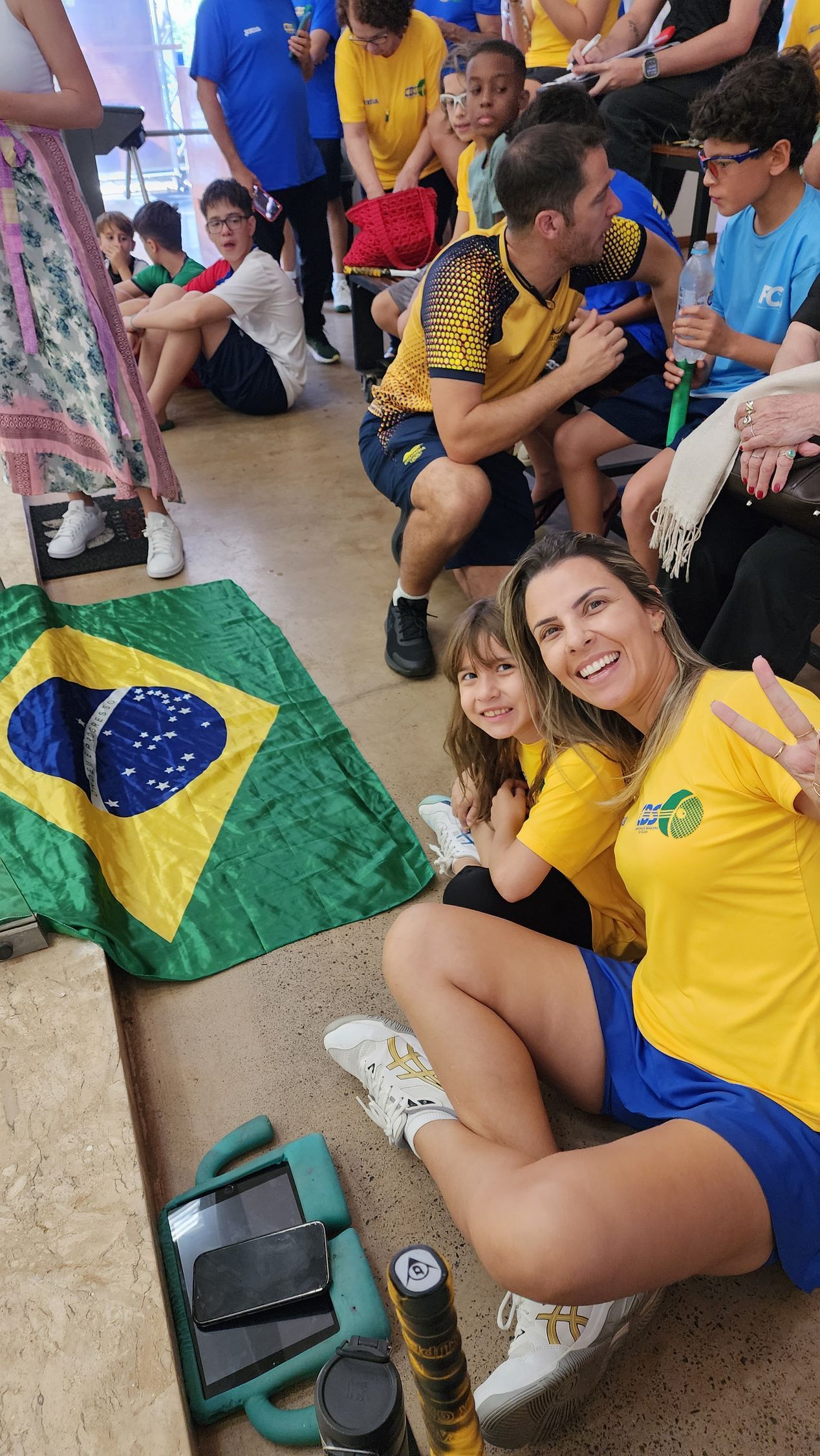 um grupo de pessoas está sentado no chão em frente a uma bandeira brasileira.