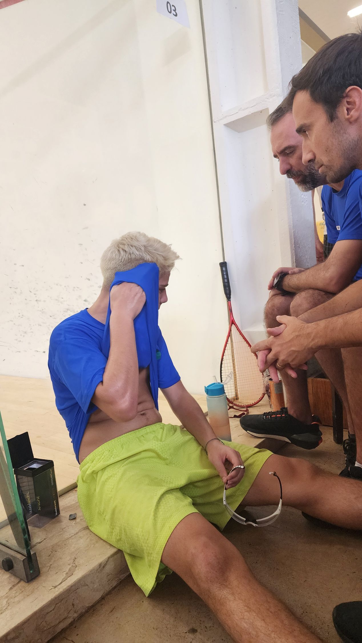um homem de camisa azul e short amarelo está sentado no chão.