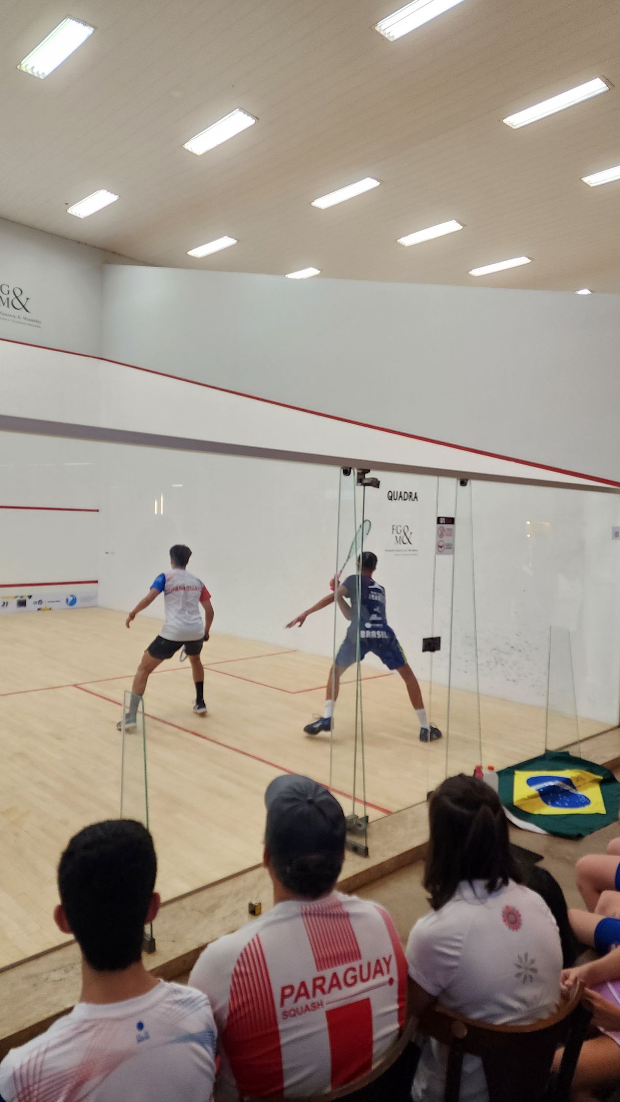 um grupo de pessoas assiste a uma partida de squash em uma academia.