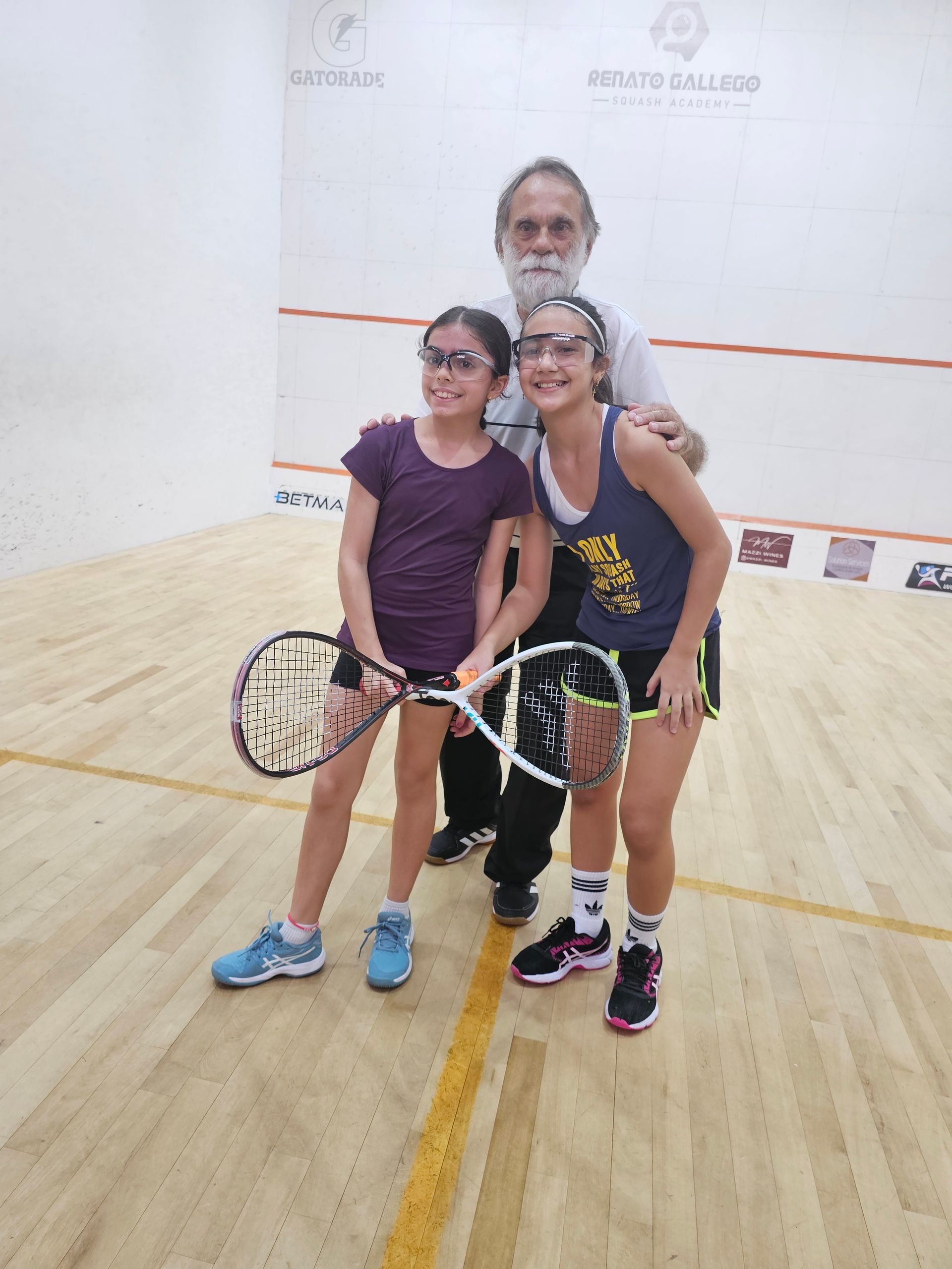 Um homem e duas meninas estão posando para uma foto em uma quadra de squash