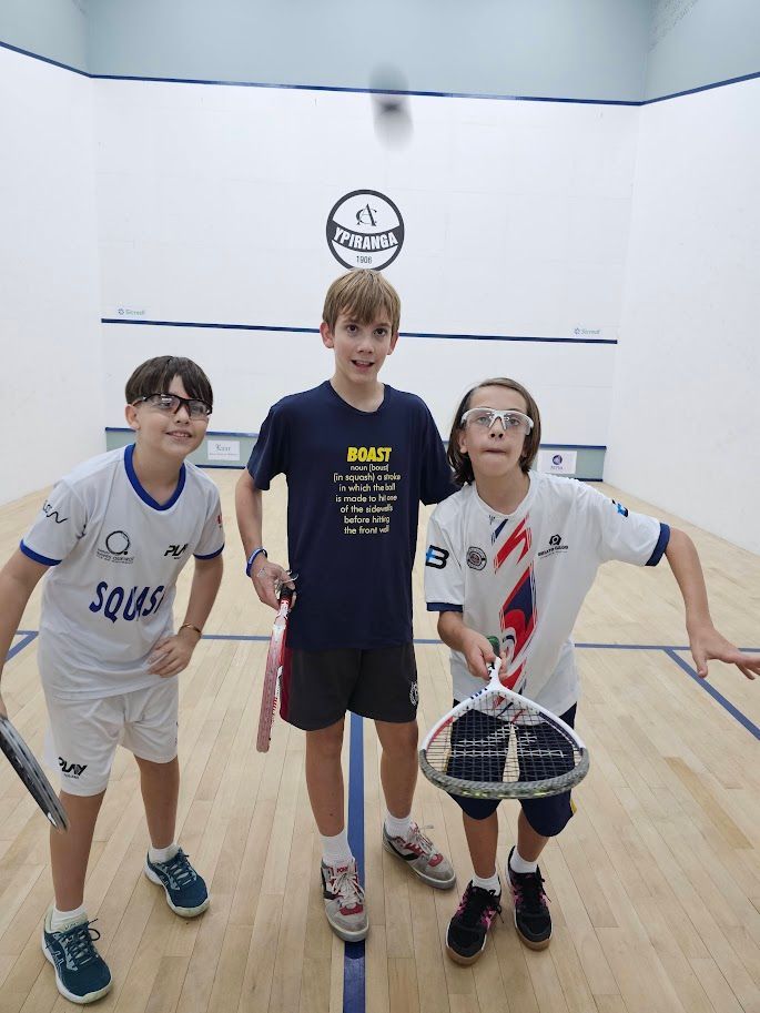 Três meninos estão posando para uma foto em uma quadra de squash