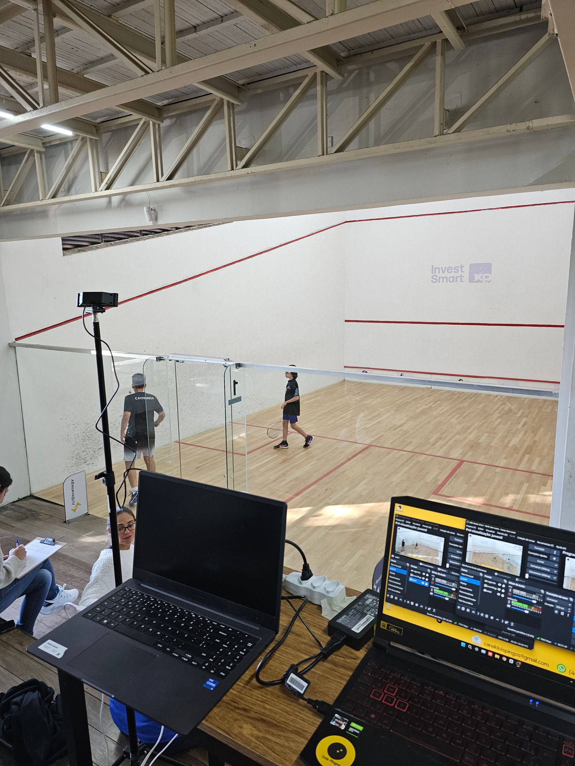 Um laptop está sobre uma mesa em frente a uma quadra de squash.