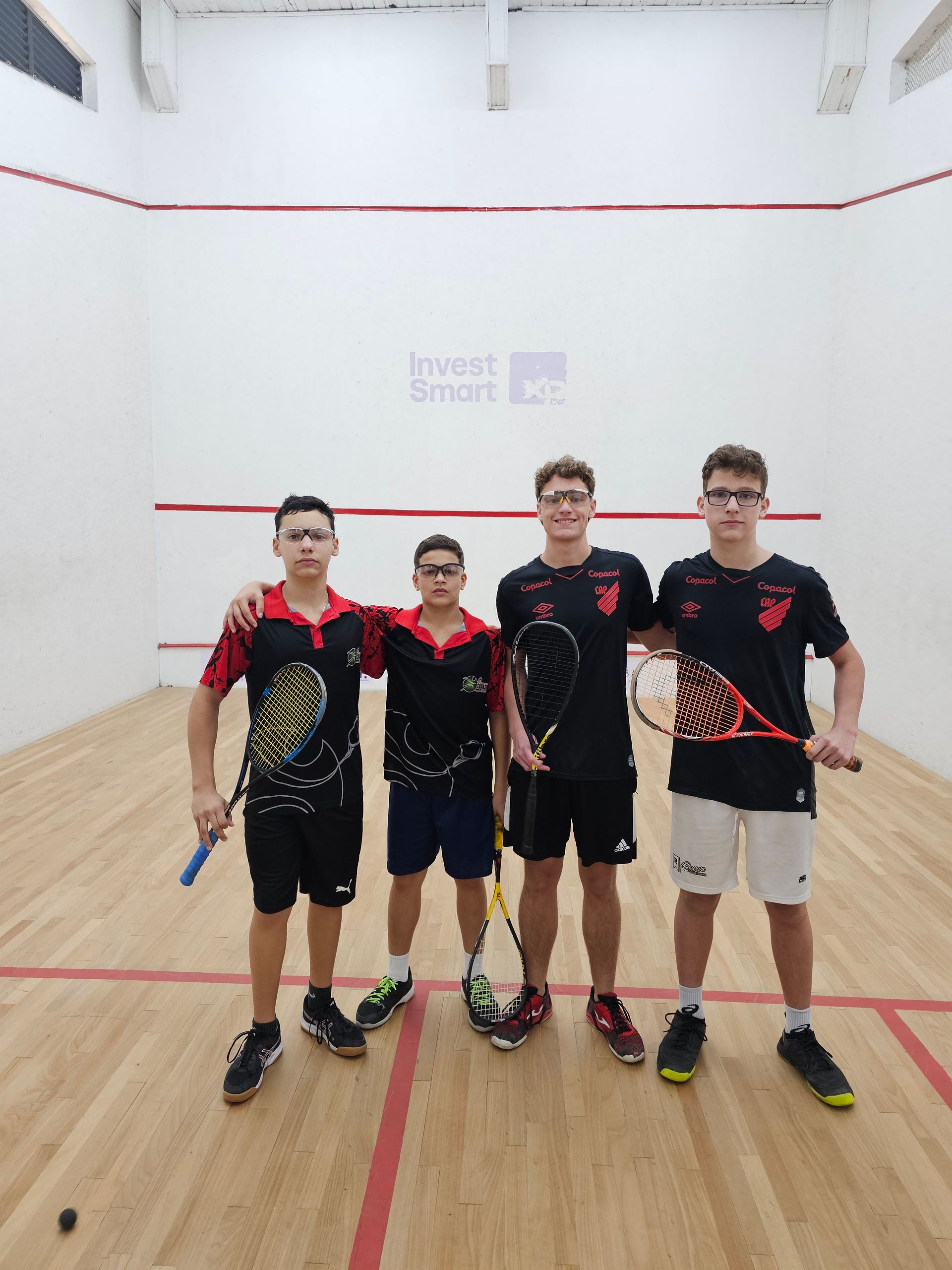 Um grupo de jovens está posando para uma foto em uma quadra de squash