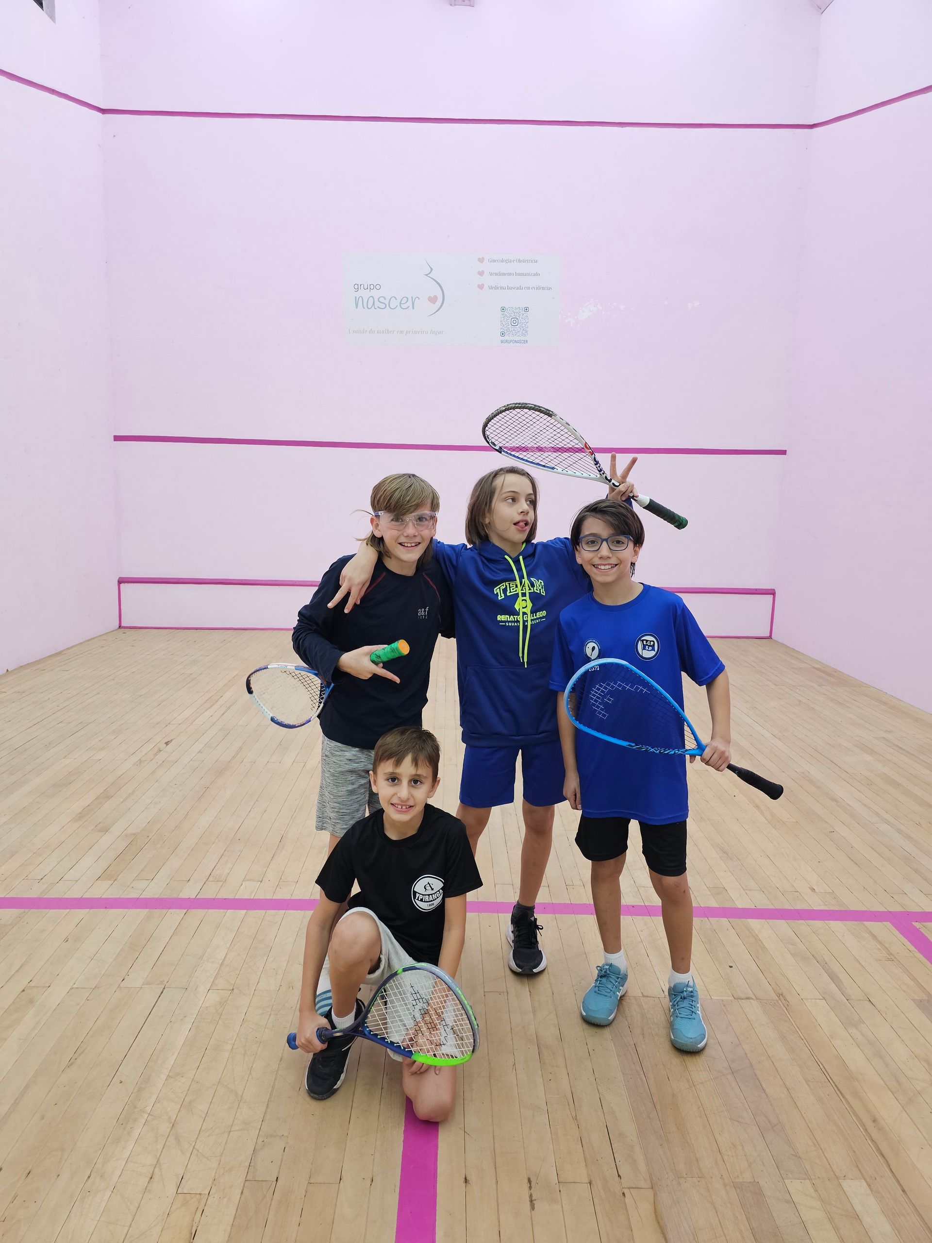 Um grupo de jovens rapazes está posando para uma foto em uma quadra de squash
