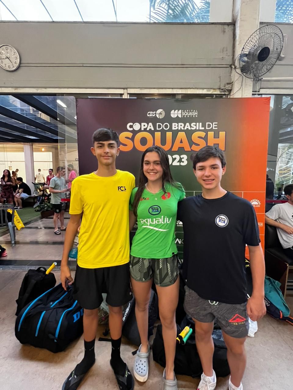Três pessoas estão posando para uma foto em frente a uma placa que diz squash.