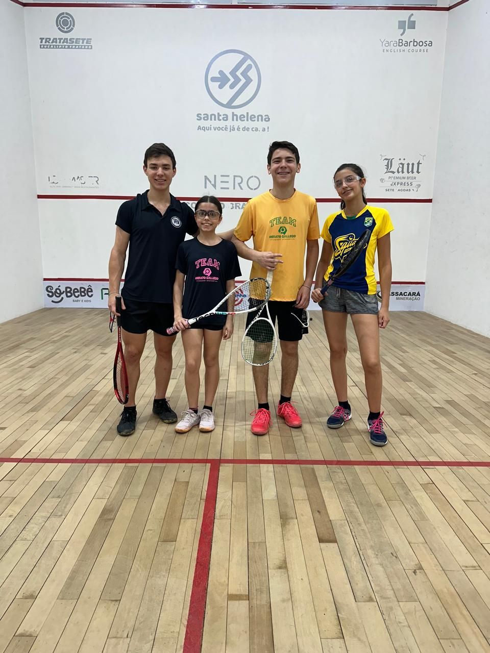 Um grupo de jovens está posando para uma foto em uma quadra de squash.