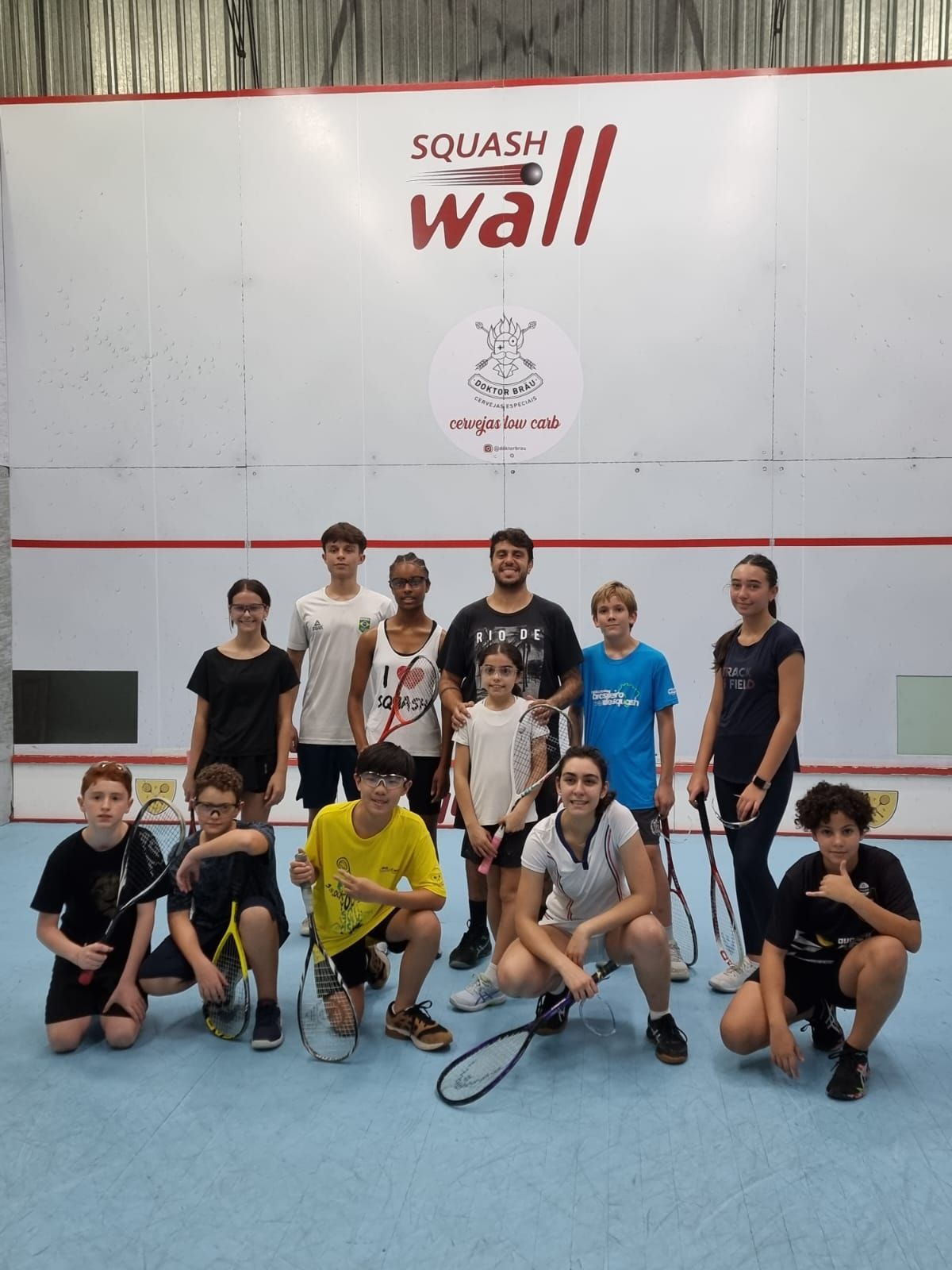 Um grupo de pessoas posando para uma foto em frente a uma placa que diz parede de squash