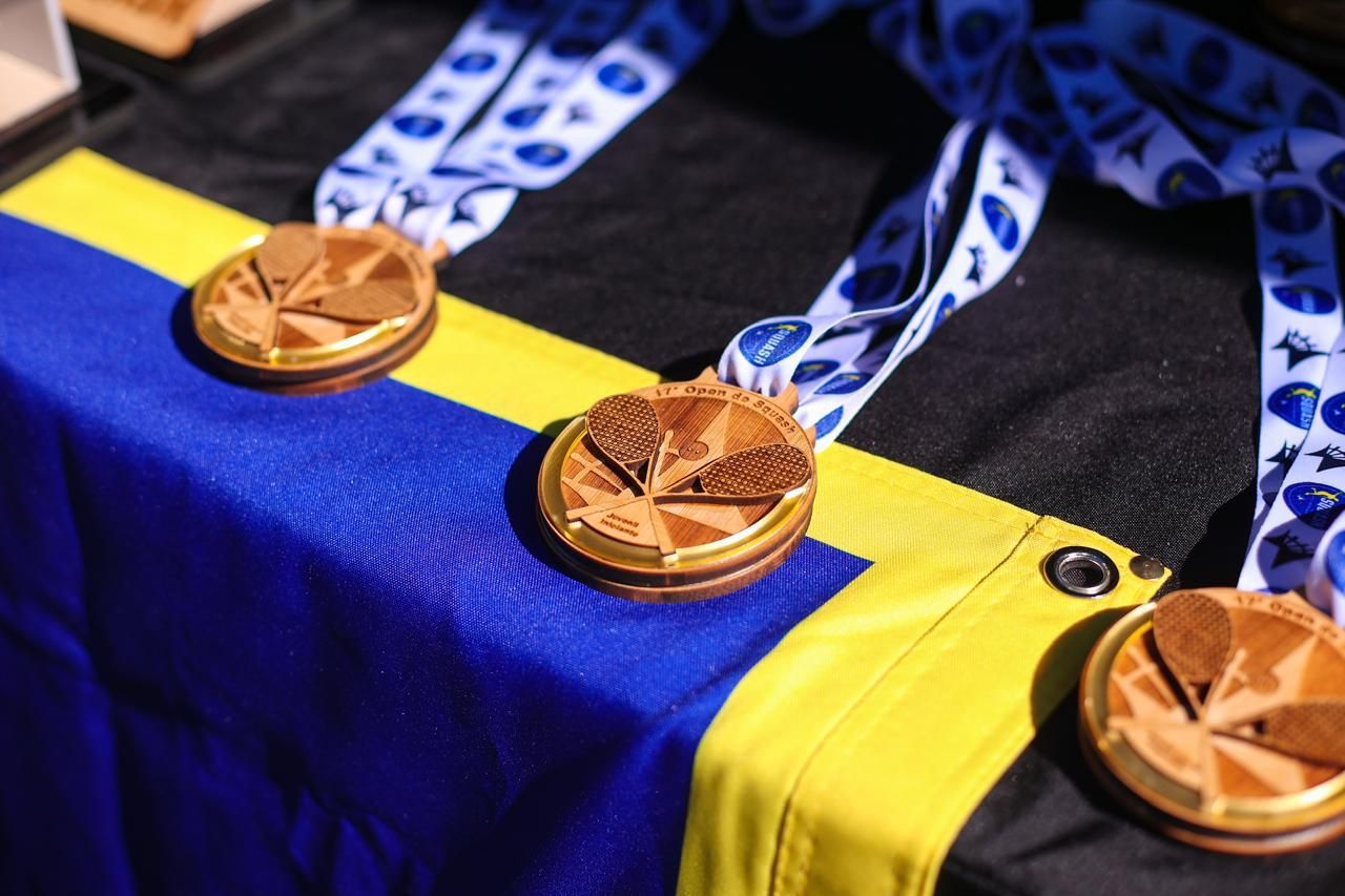 Três medalhas de ouro estão sobre uma toalha de mesa azul e amarela.