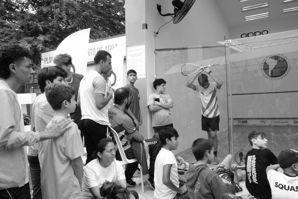 Uma foto em preto e branco de um grupo de pessoas assistindo a um jogo de squash