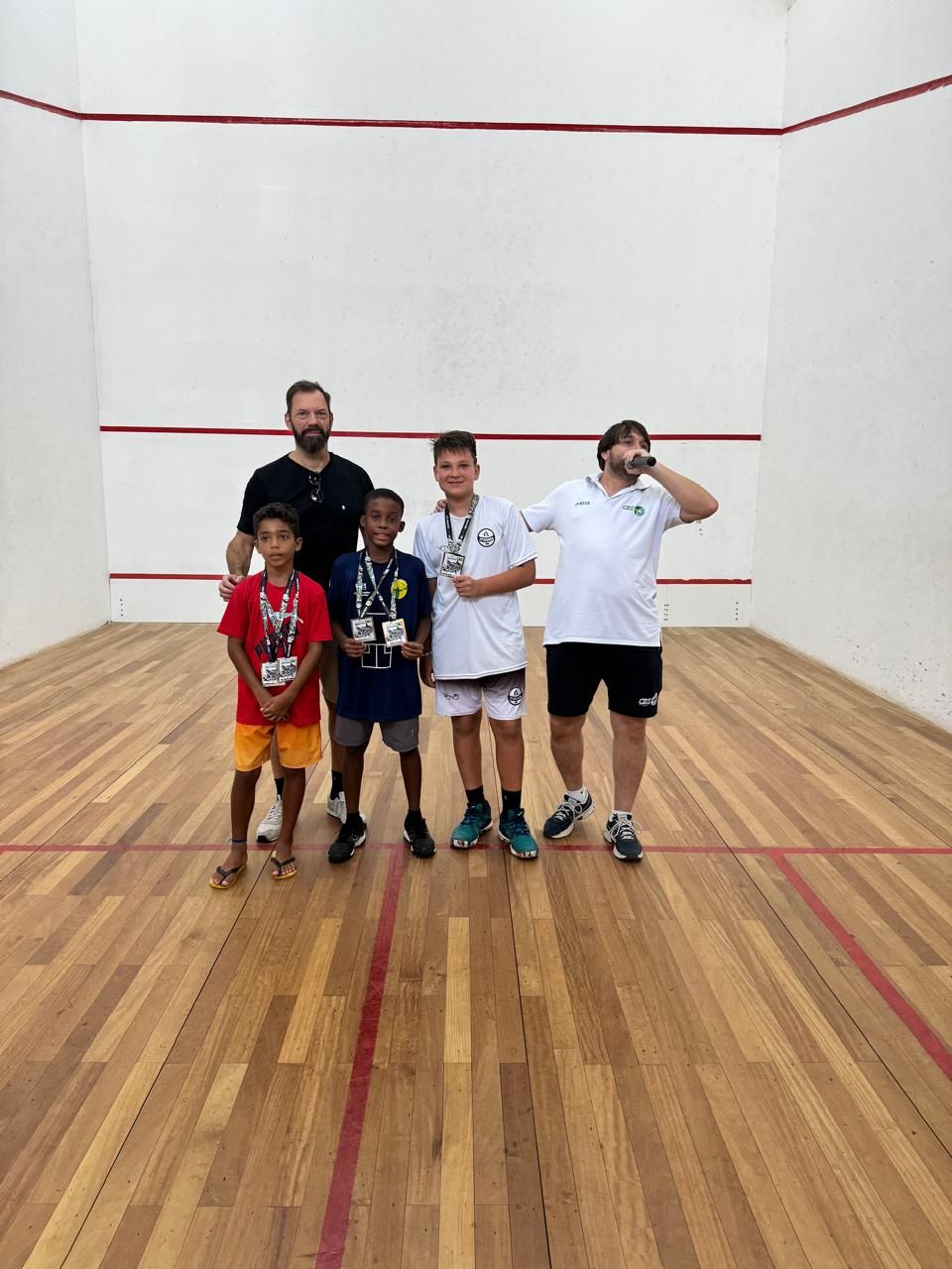 Um grupo de pessoas está posando para uma foto em uma quadra de squash.