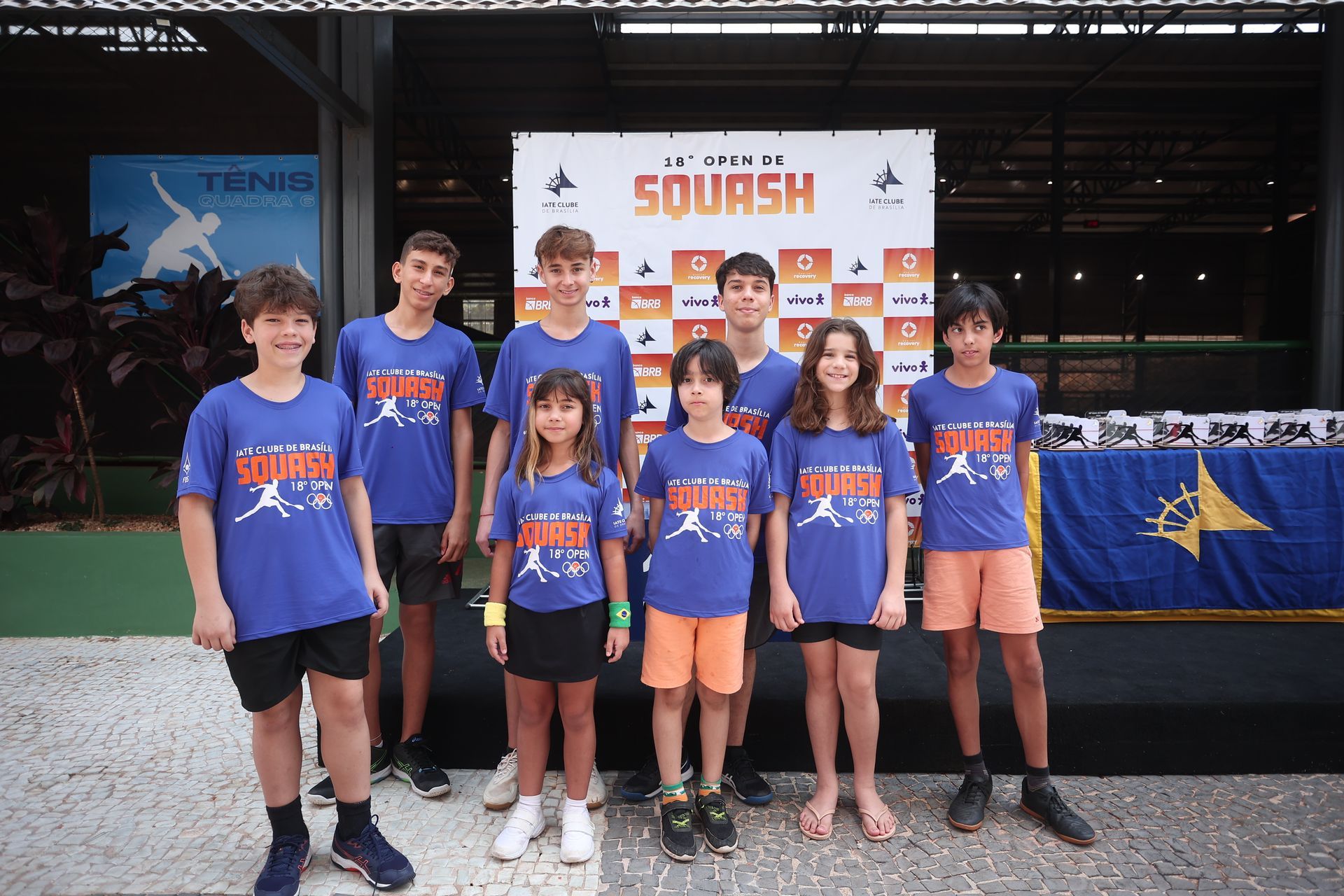 Um grupo de crianças está posando para uma foto em frente a uma placa que diz squash.