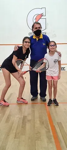 Um homem e duas meninas estão posando para uma foto em uma quadra de squash.