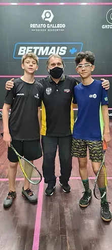 Um homem e dois meninos estão posando para uma foto em uma quadra de squash.