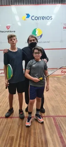Um homem e dois meninos estão posando para uma foto em uma quadra de squash.
