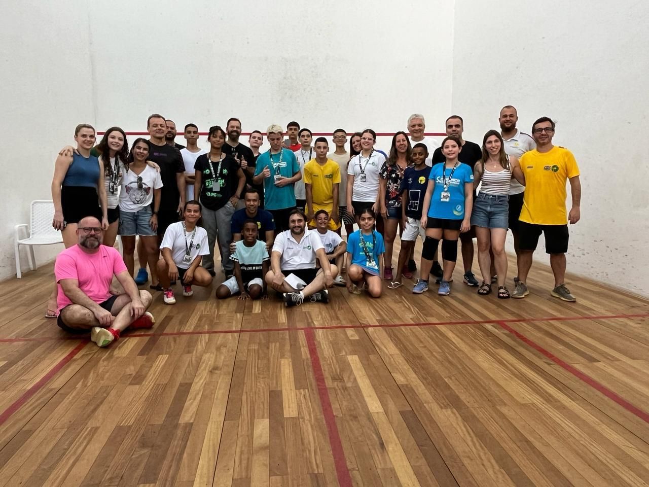 Um grupo de pessoas está posando para uma foto em uma quadra de squash.