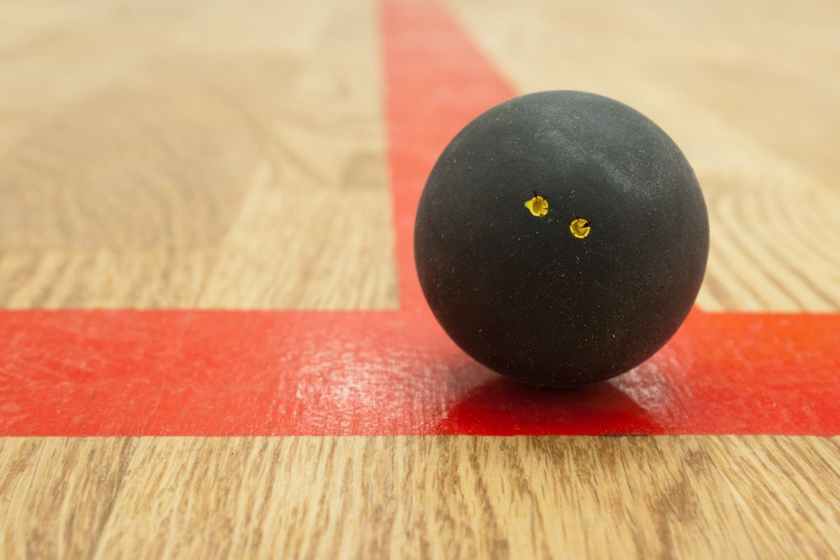 Uma bola de squash está sobre uma quadra de madeira ao lado de uma linha vermelha.