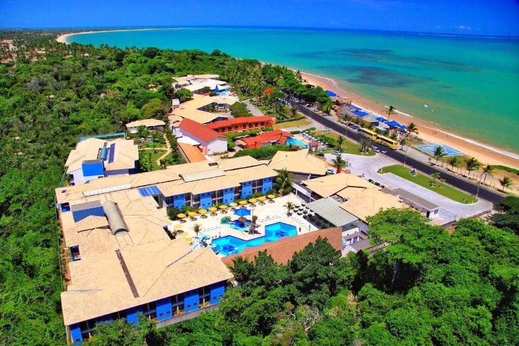 Uma vista aérea de um hotel cercado por árvores e uma praia.