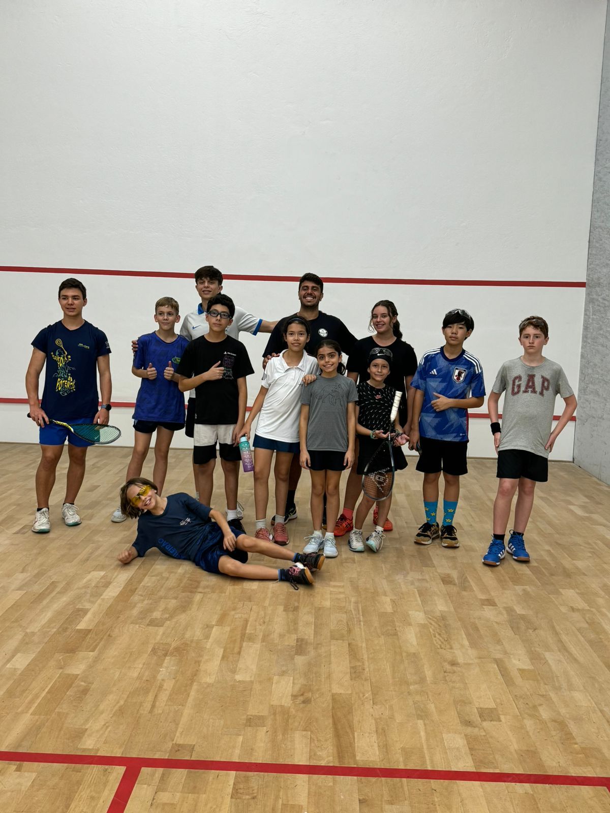 Um grupo de jovens está posando para uma foto em uma quadra de squash.