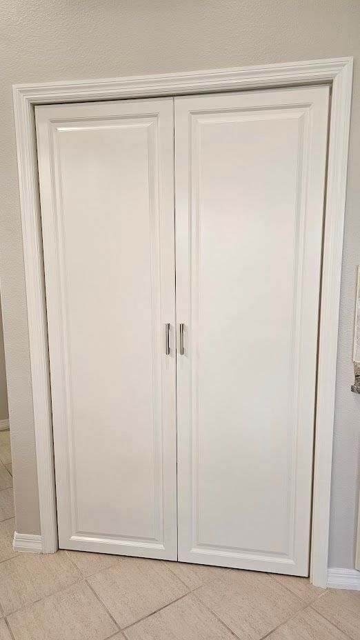 A pair of white cabinet doors in a room with tile floors.
