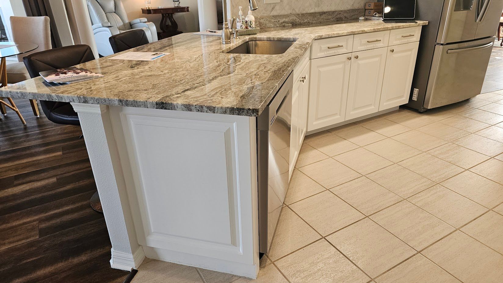 A kitchen with granite counter tops , white cabinets , a stainless steel refrigerator , and a sink.