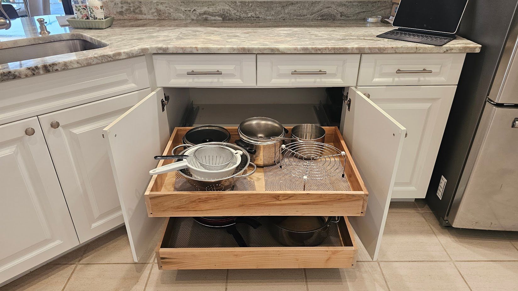 A kitchen with a pull out drawer filled with pots and pans.