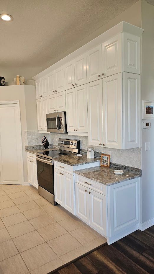 A kitchen with white cabinets , granite counter tops , and stainless steel appliances.