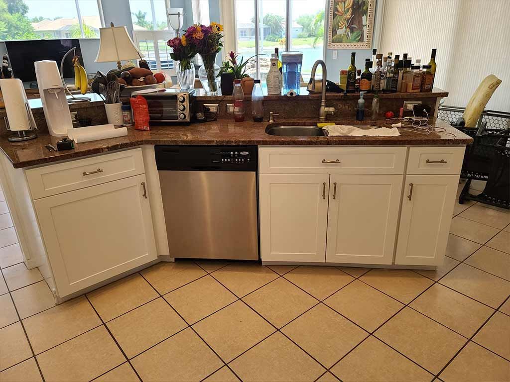 A kitchen with white cabinets , a stainless steel dishwasher , a sink and a microwave.
