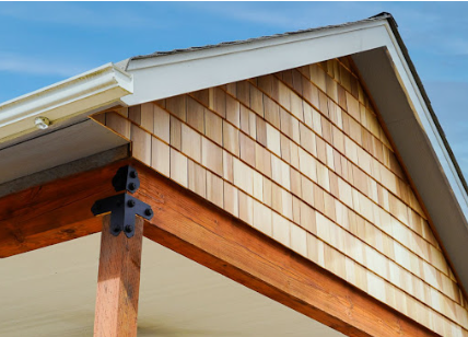 Wooden shingles on a house's gable, with a white fascia and brown wooden beam.