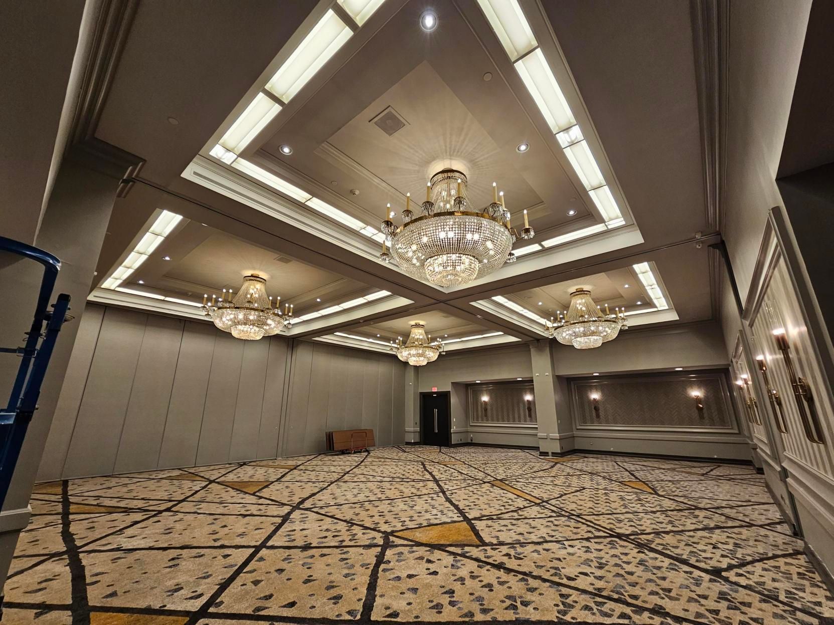 Empty ballroom with chandeliers, patterned carpet, and recessed ceiling lights.