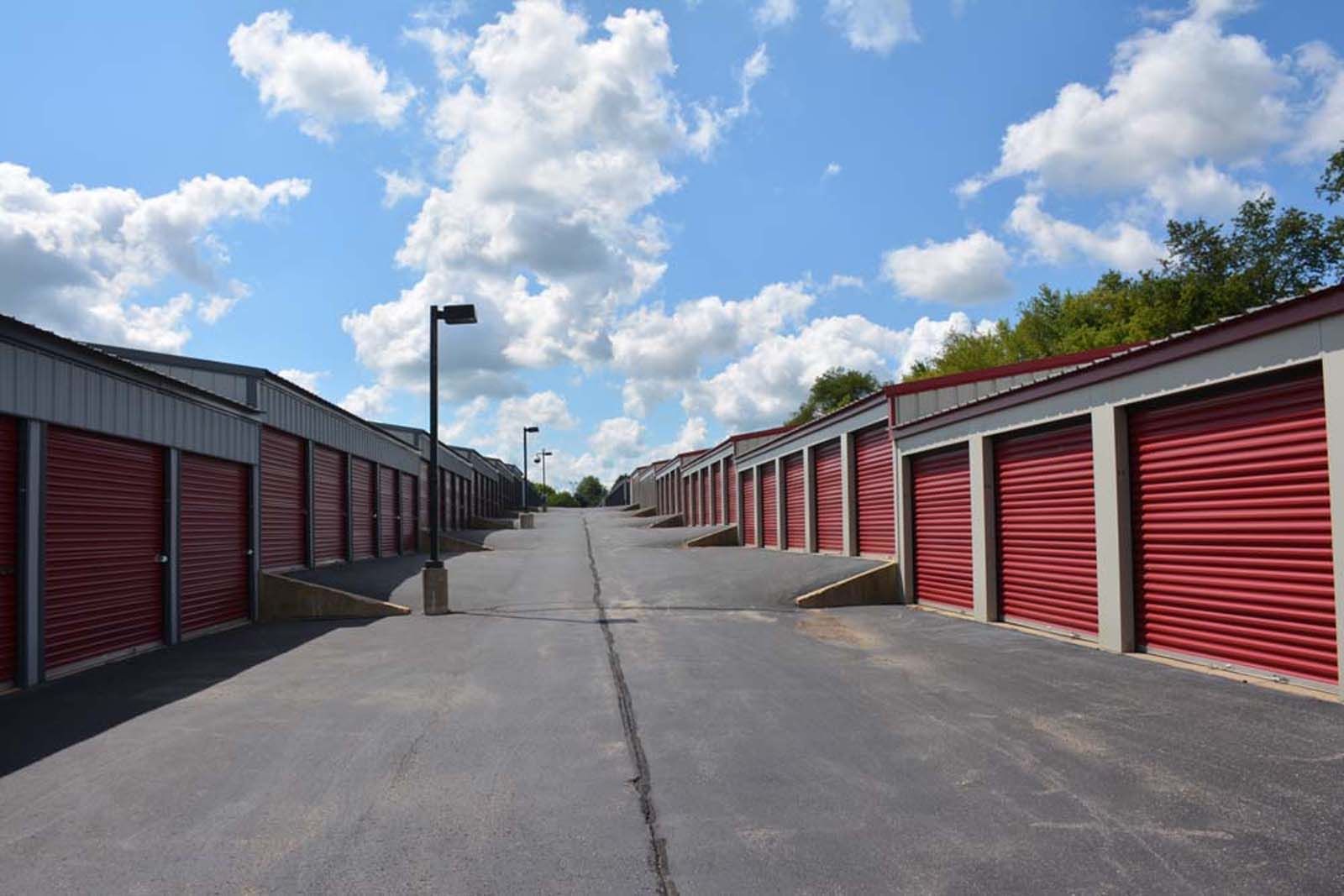 Storage unit rows lining a paved lane under a blue sky with clouds