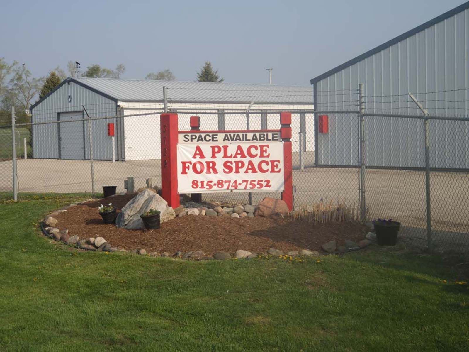 Storage facility entrance with sign reading “A Place for Space” beside metal buildings and a fence.