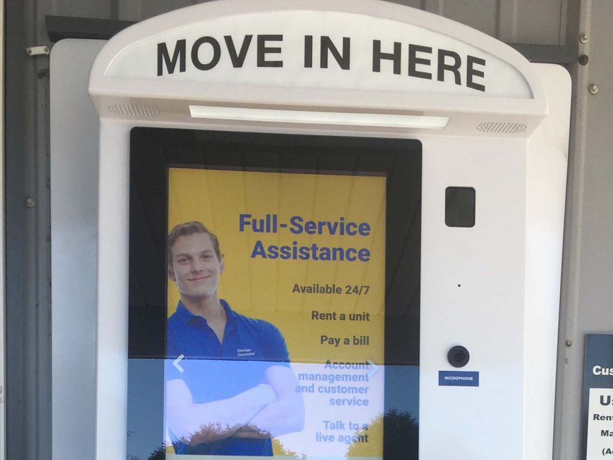 White kiosk with “MOVE IN HERE” sign and poster for full-service assistance above a service window