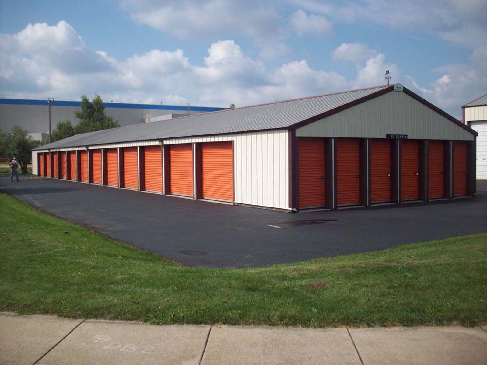 Row of orange storage units with white trim in a paved lot beside grass under a cloudy sky