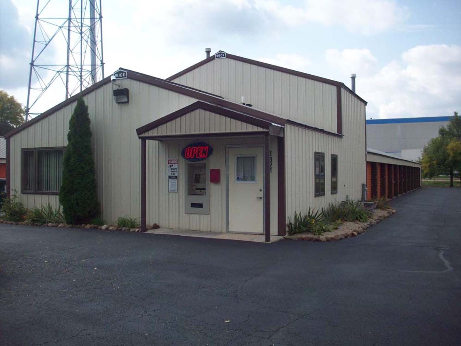 Small beige utility building with a red awning and sign, beside a paved lot and tall tower.