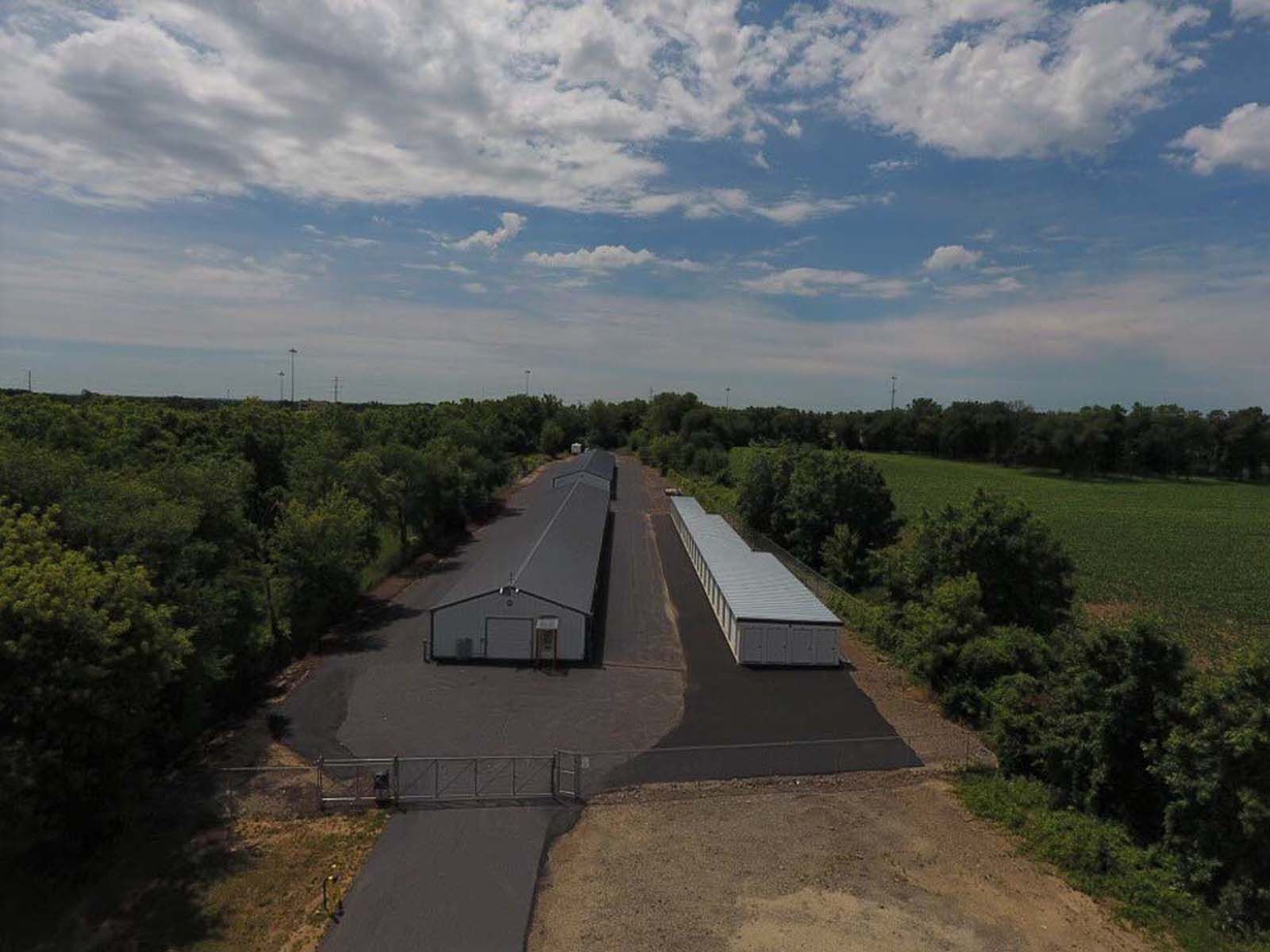 Aerial view of two long warehouse buildings surrounded by trees under a partly cloudy sky