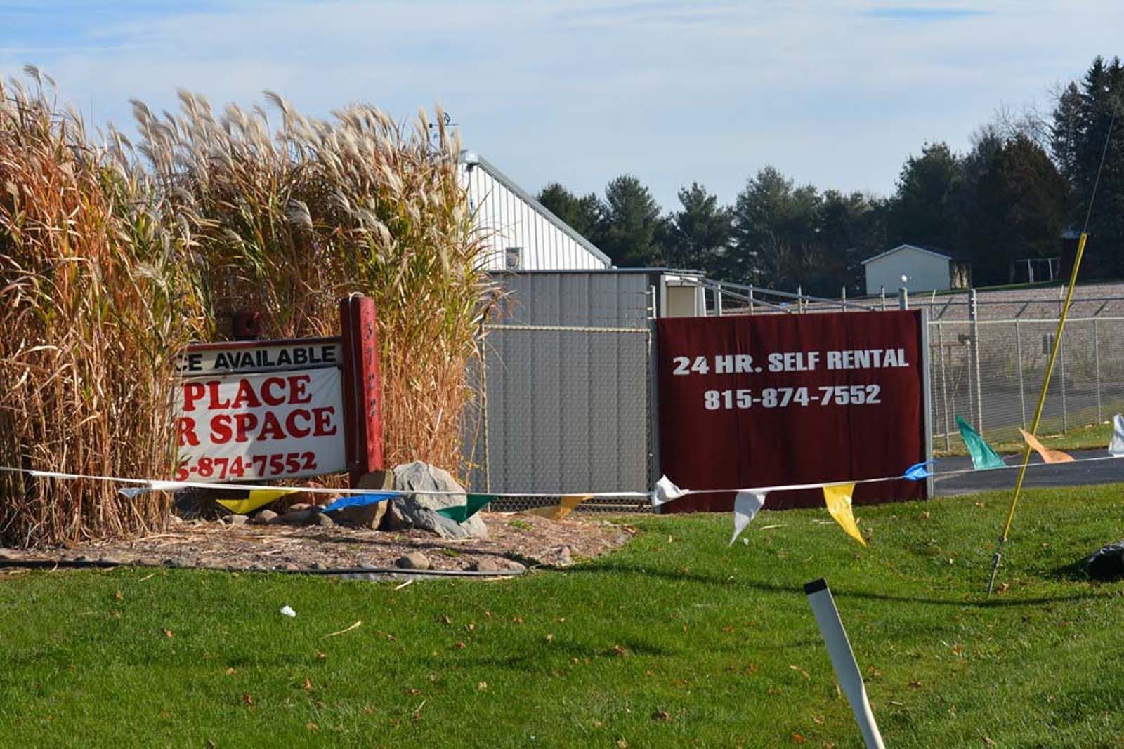 Rental storage units behind fence with signs for space rental and 24-hour self storage