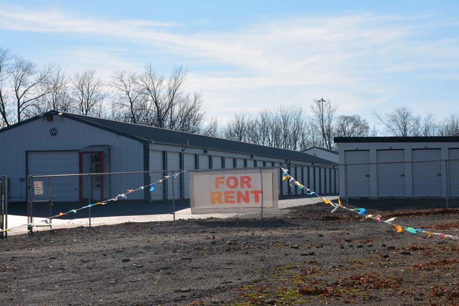 Vacant building with a “FOR RENT” sign in front, under a clear sky.