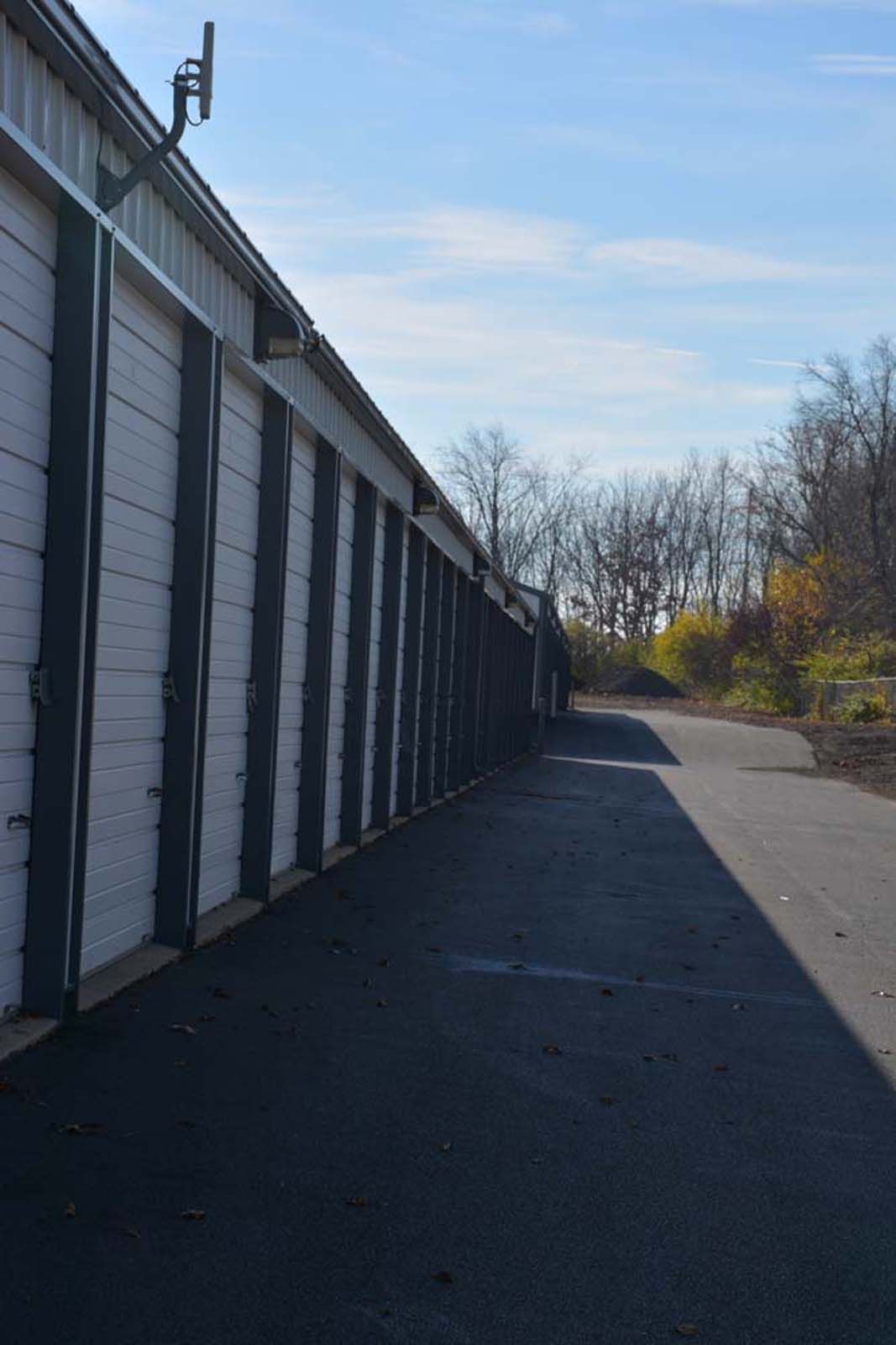 Row of white storage unit doors beside a paved driveway on a clear day
