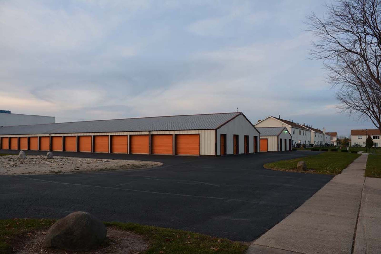 Row of orange storage units beside a paved lot and sidewalk under a cloudy sky