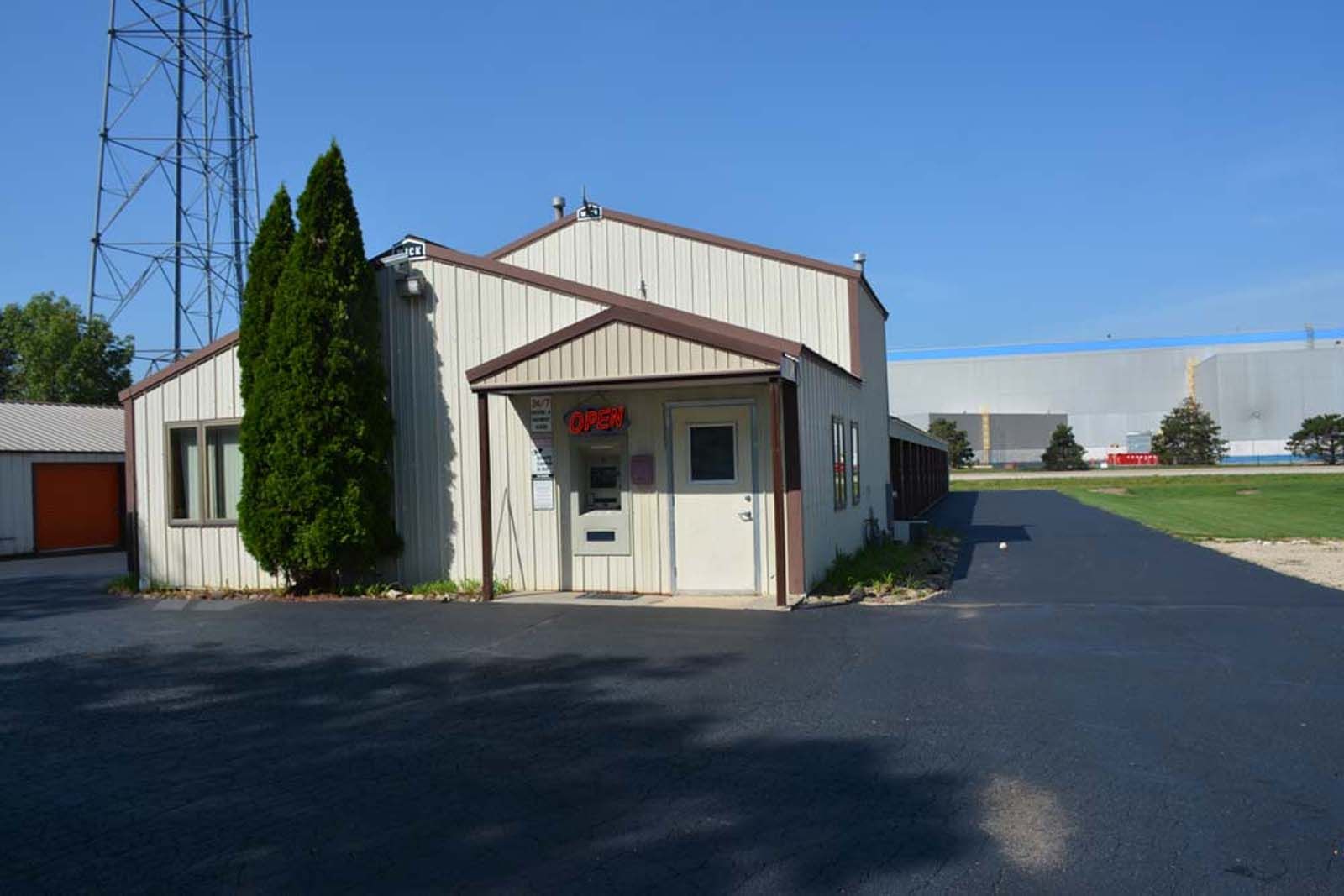 Small beige building with a red trim entrance on a paved lot under a clear blue sky.