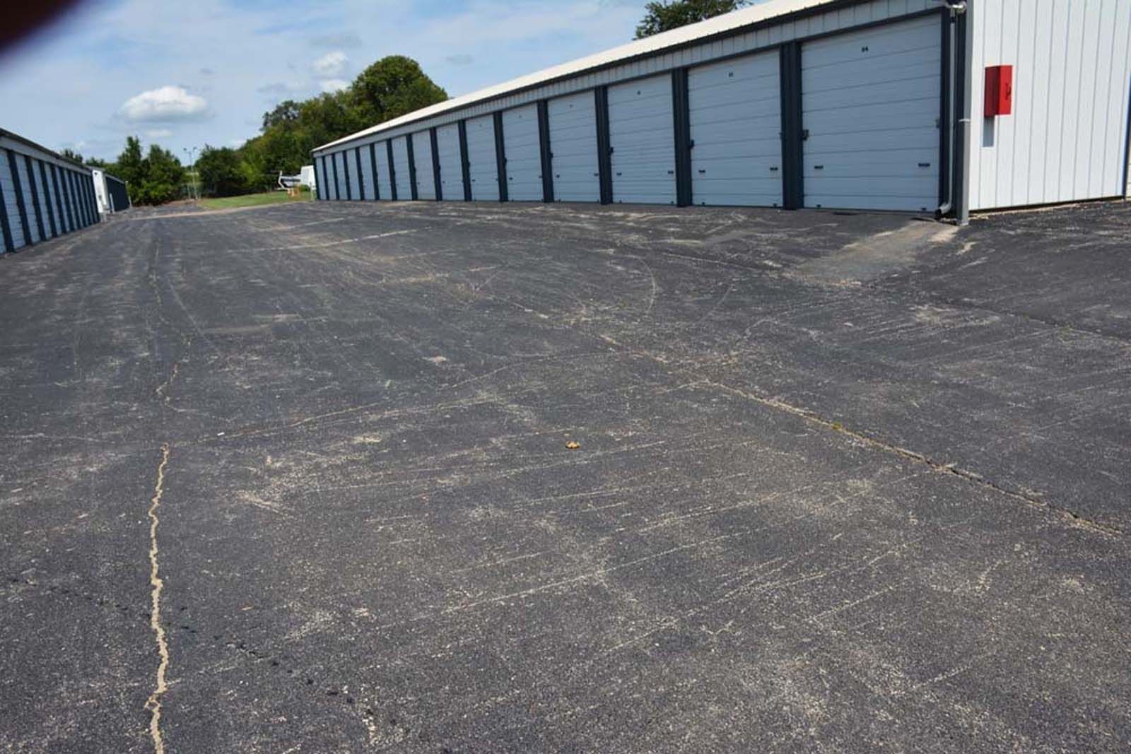 Row of white storage units with blue doors beside a wide asphalt lot under a blue sky