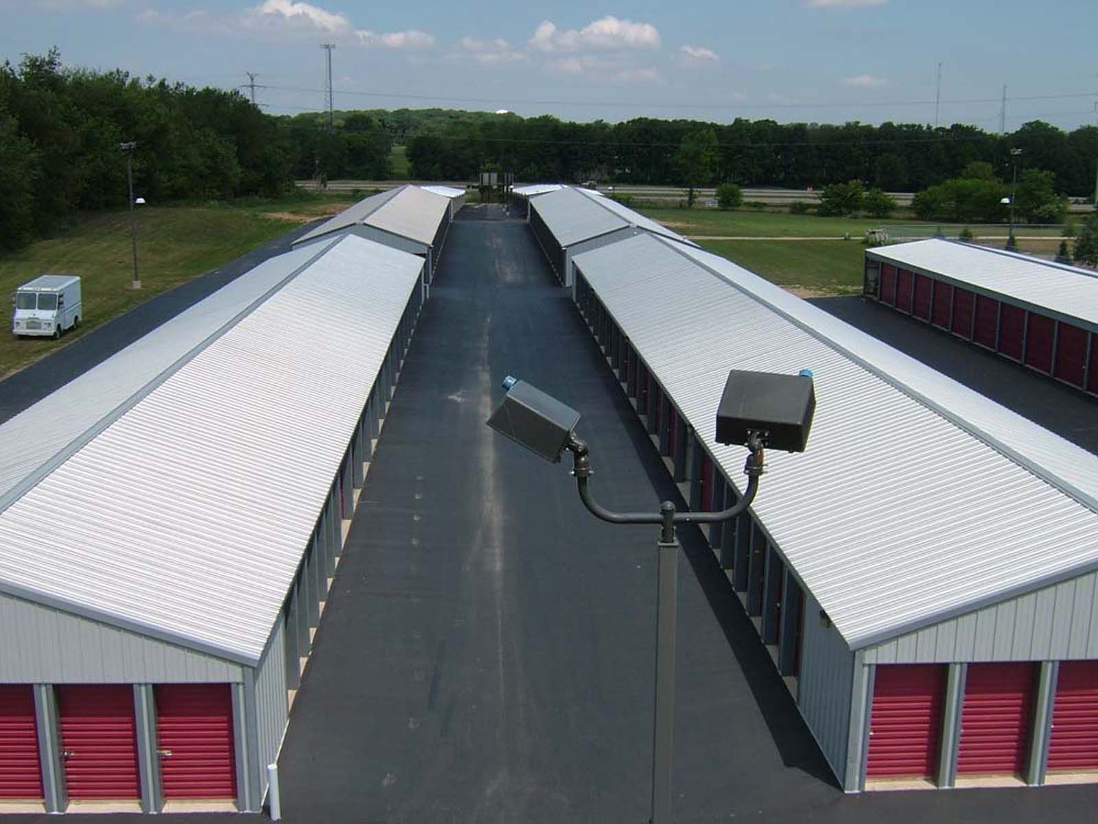 Aerial view of two long white-roofed buildings with red doors and a central paved corridor.