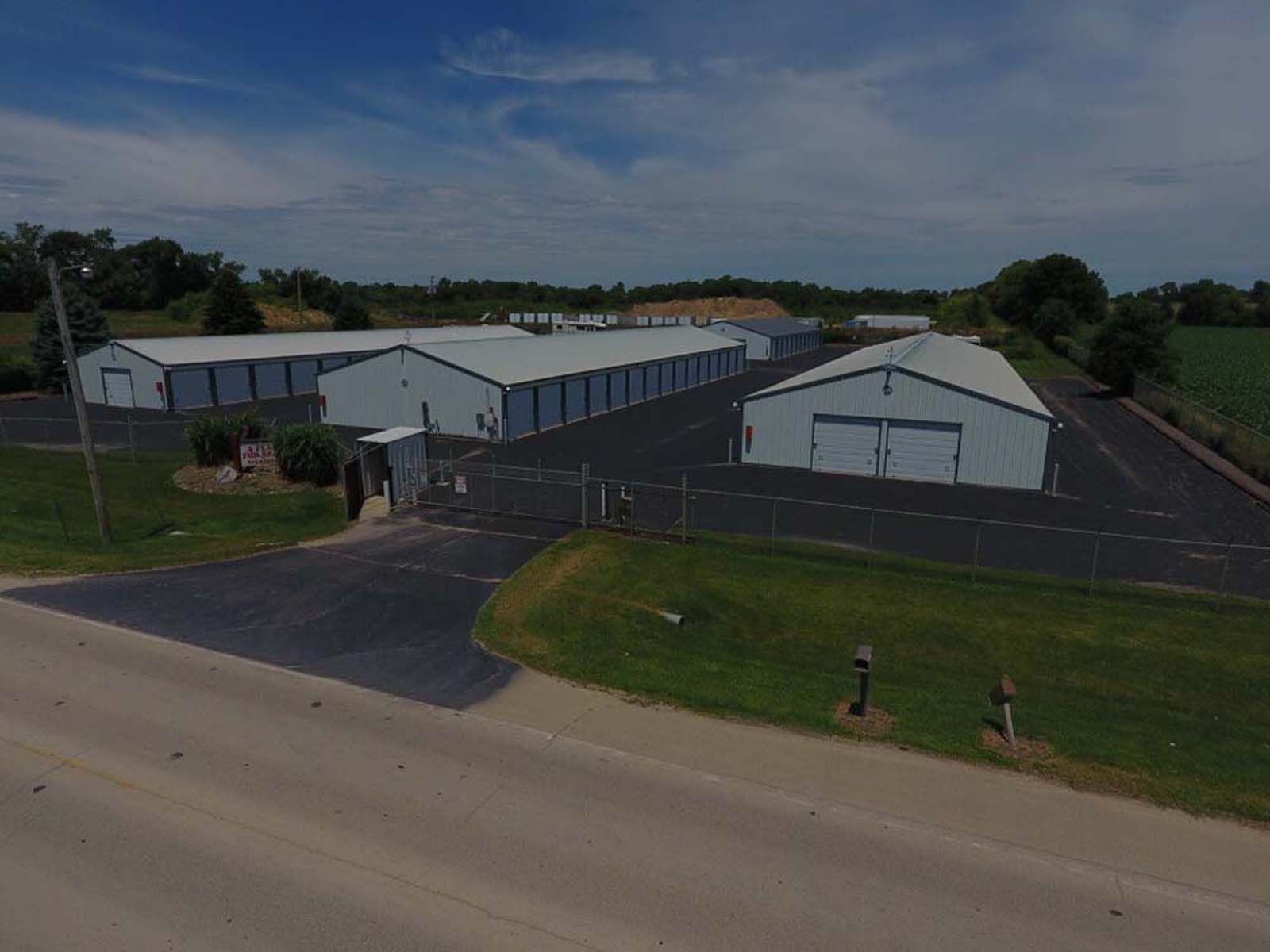 Aerial view of a large gray industrial building with a paved lot beside a rural road.