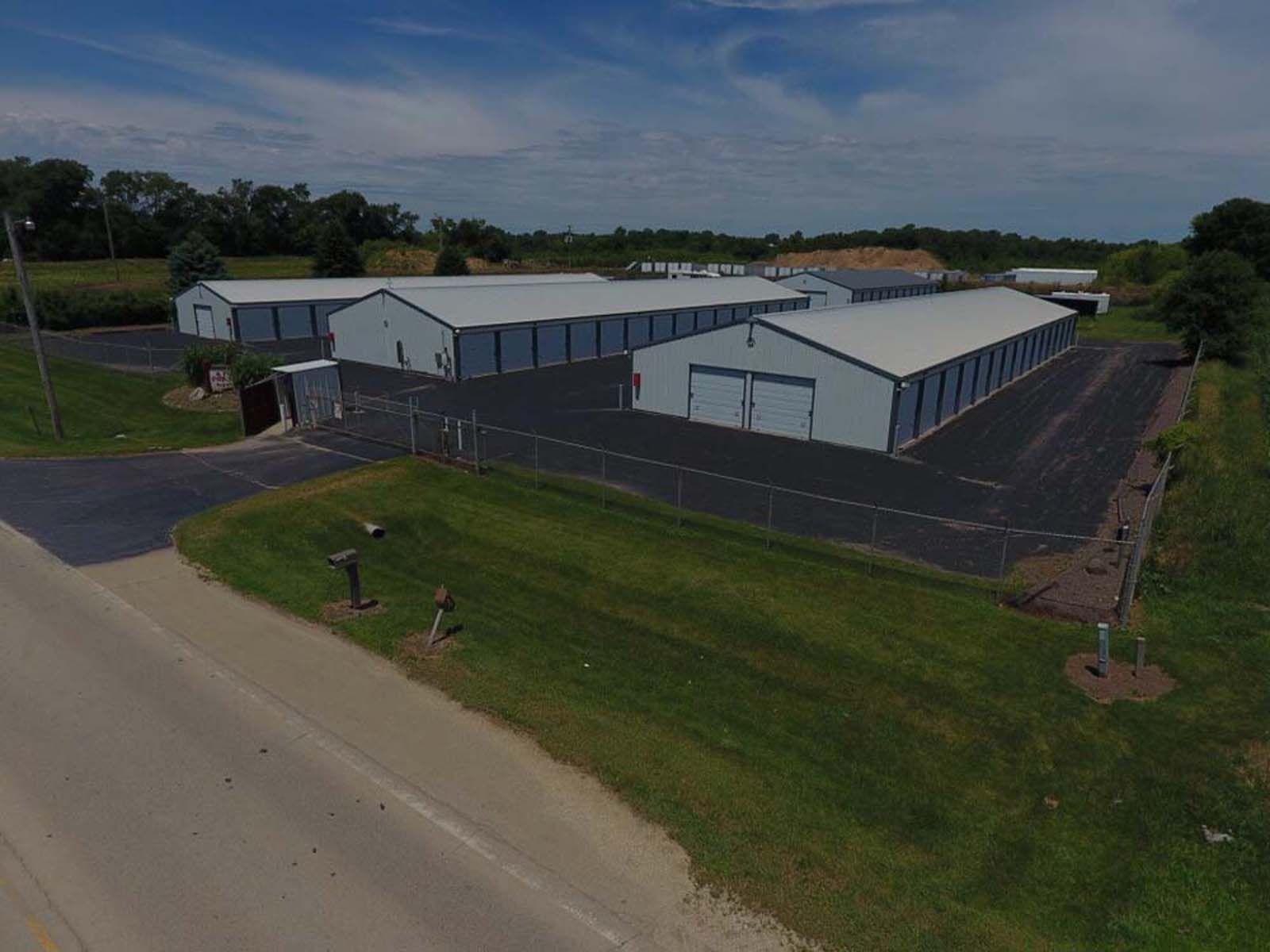 Aerial view of a large white warehouse complex beside a road and grassy lot under cloudy skies