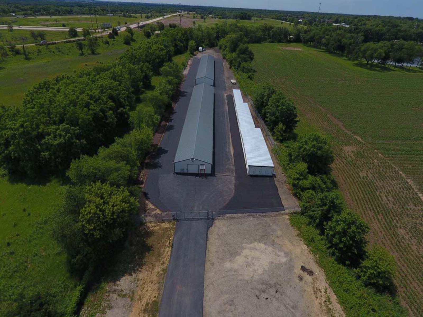Aerial view of two long white trucks parked on a paved road beside green fields.