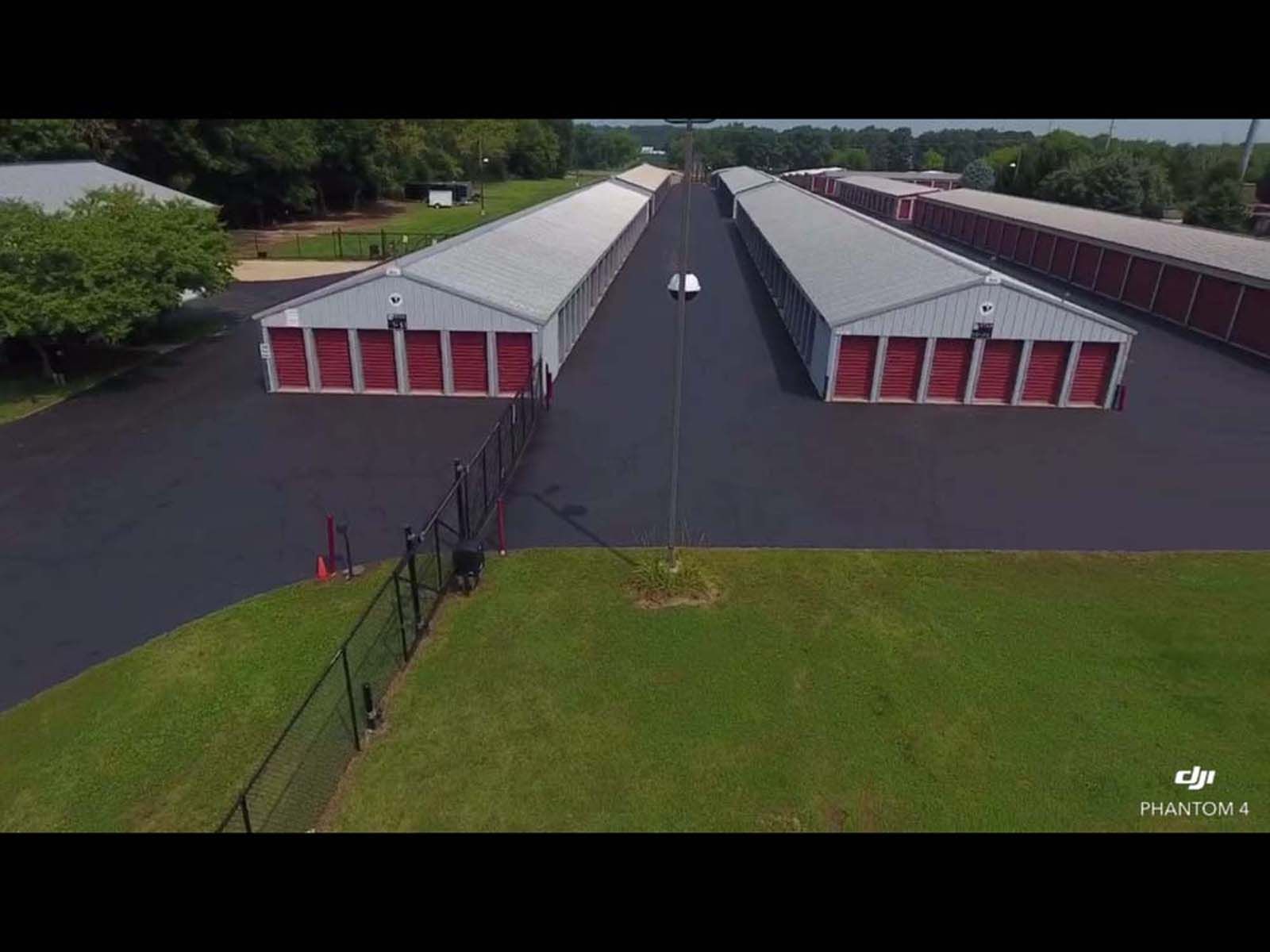 Aerial view of a long row of red-and-white storage units on paved ground beside green grass.