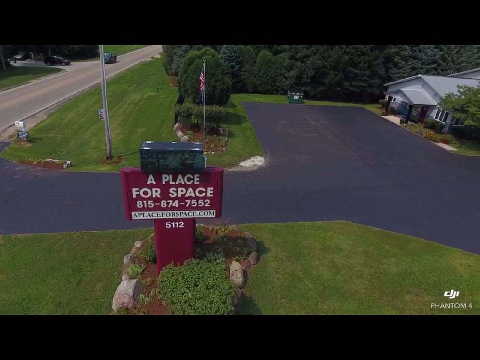 Roadside “Place for Space” sign by a driveway and building, surrounded by grass and trees