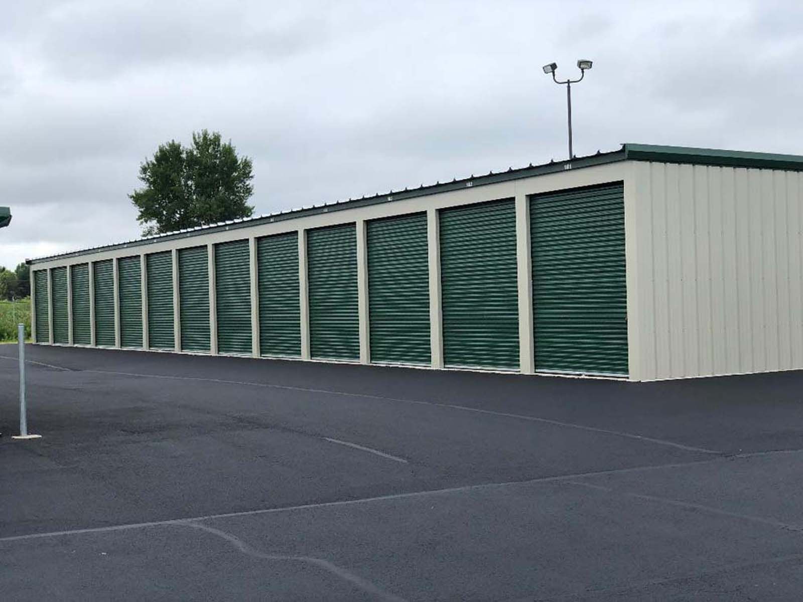 Row of green storage unit doors in a paved outdoor lot under a cloudy sky
