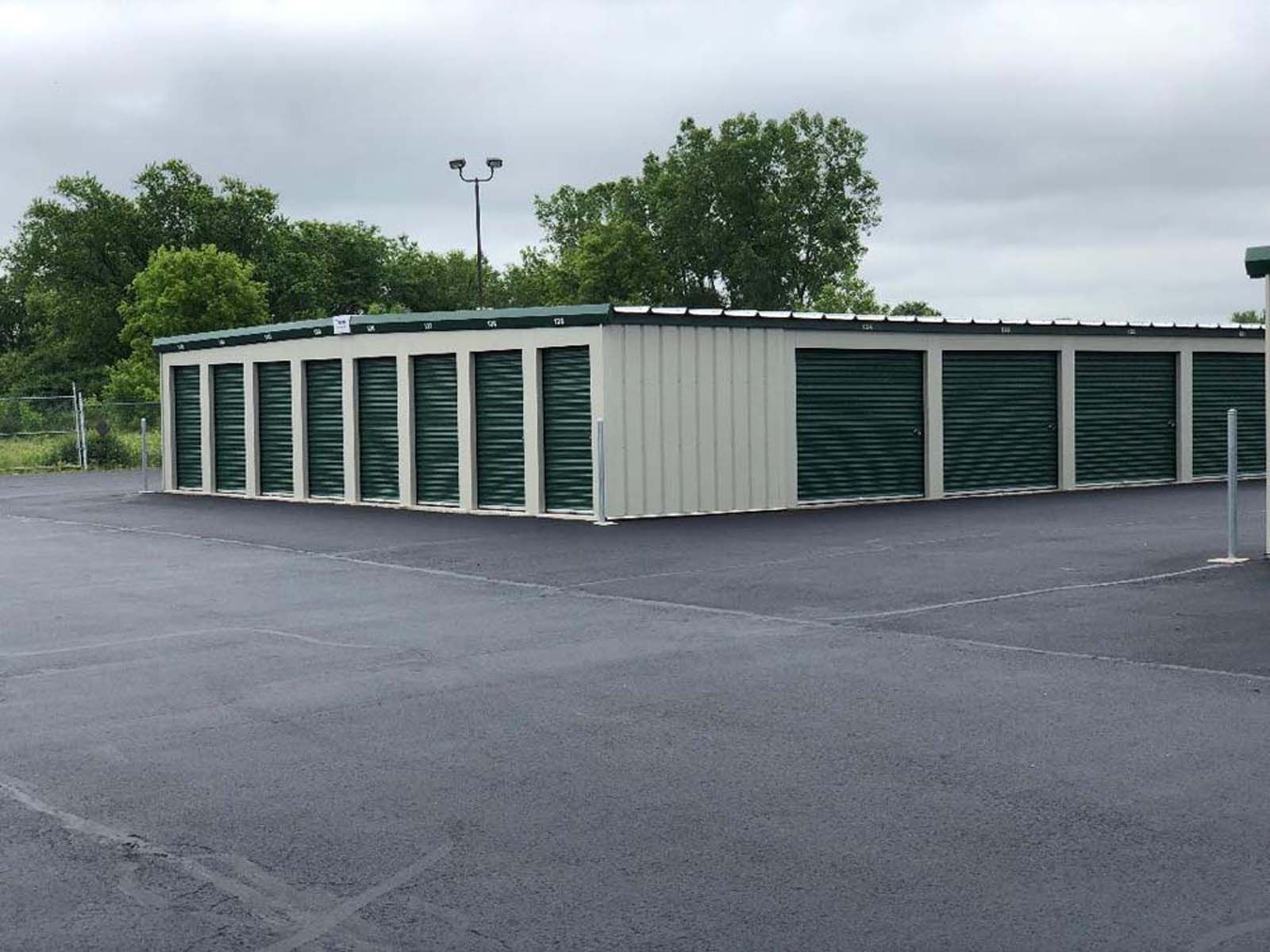 Row of beige and green storage units on an empty asphalt lot under cloudy skies
