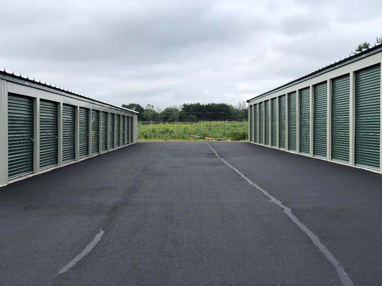 A paved path between two rows of storage units under a cloudy sky.